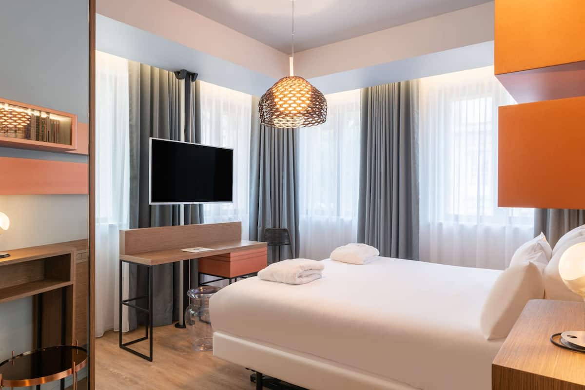 Ein modernes Hotelzimmer mit einem großen Bett, einem Schreibtisch, einem Fernseher und einer außergewöhnlichen Pendelleuchte.