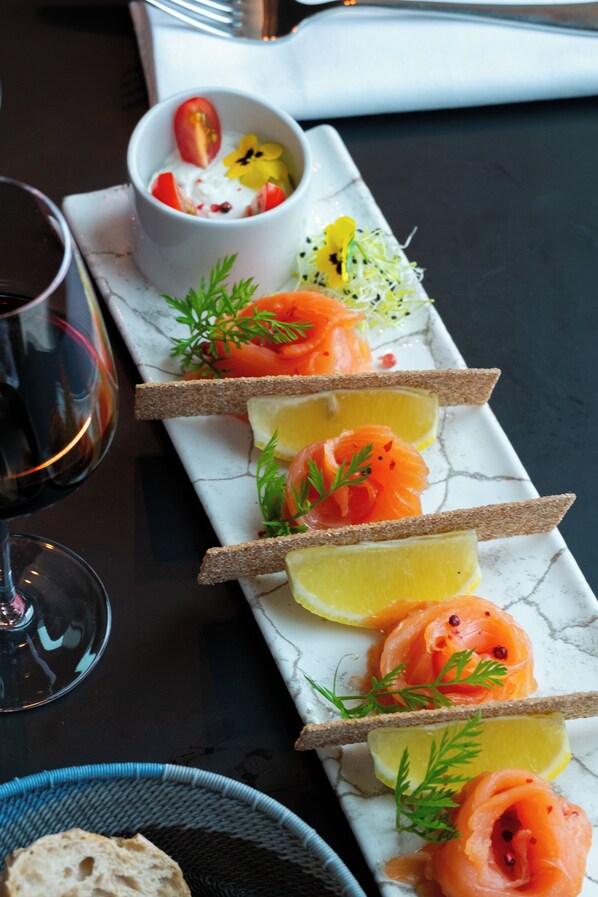 A table with a white plate holding salmon and lemon slices, a bowl of yogurt with fruit, and a glass of red wine.