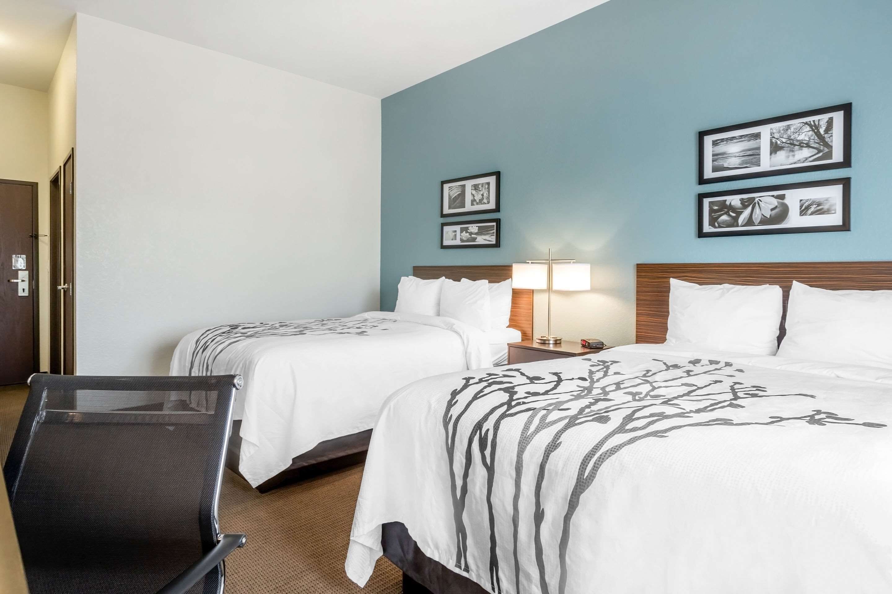 A hotel room with two beds, a desk, and a chair. There are framed pictures on the wall.