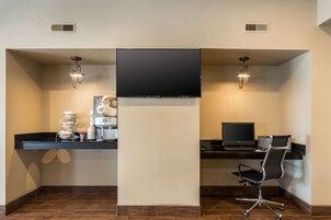 Un espacio de oficina moderno con una televisión de pantalla plana montada en un pilar central, dos escritorios con computadoras, una silla de oficina negra y una estación de café.