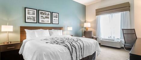 A hotel room with a large bed, two bedside tables with lamps, a chair, a desk, and a large window with curtains.