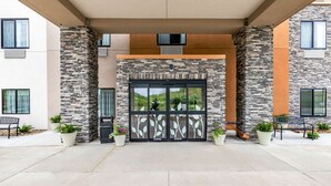 A building entrance with a stone facade, large glass doors, and potted plants.