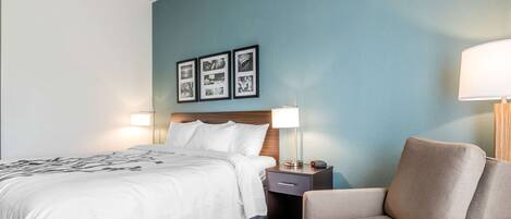 A hotel room with a bed, bedside table, lamp, and a chair.