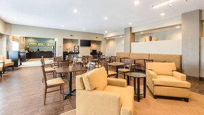 A spacious lobby with multiple seating areas, including sofas and tables, and a visible kitchen area in the background.