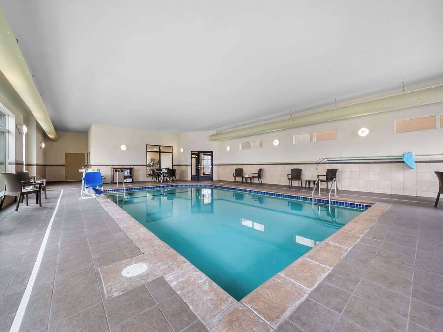 An indoor swimming pool with tiled flooring, seating areas, and a door leading to another room.