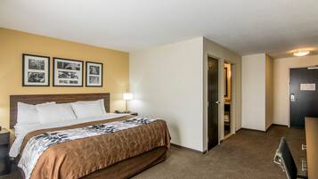 A hotel room with a bed, bedside table, lamp, and a wall with framed pictures.