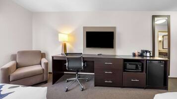 A hotel room with a bed, a desk with a chair, a flat-screen TV, a microwave, a refrigerator, a lamp, and a mirror.