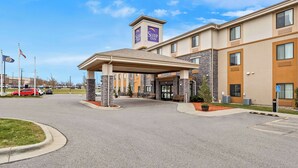 Ett Sleep Inn-hotell med en inglasad entré, stenkantade pelare och en klarblå himmel.