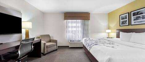 Una habitación de hotel con cama, escritorio, silla, televisor y dos lámparas.