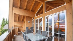 A wooden deck with a glass table and chairs, large windows, and a view of the surrounding area. - Luxury apartment in Brixen (Brixen im Thale)