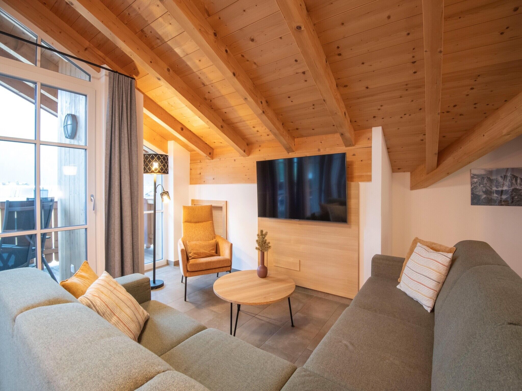 Ein gemütliches Wohnzimmer mit Holzbalkendecke, einem großen Fernseher und einem Sofa.