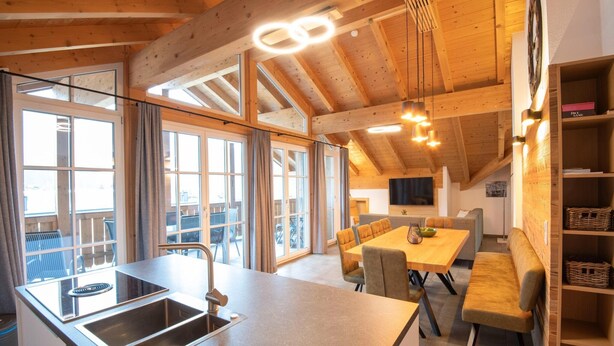 A modern kitchen with a large island, a dining area with a bench, and a wooden ceiling with exposed beams. - Luxury apartment in Brixen (Brixen im Thale)