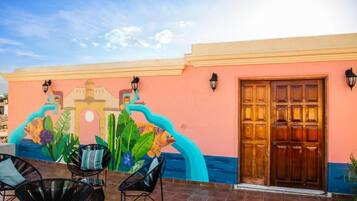 Un edificio con un mural, una puerta de madera y mesas al aire libre.