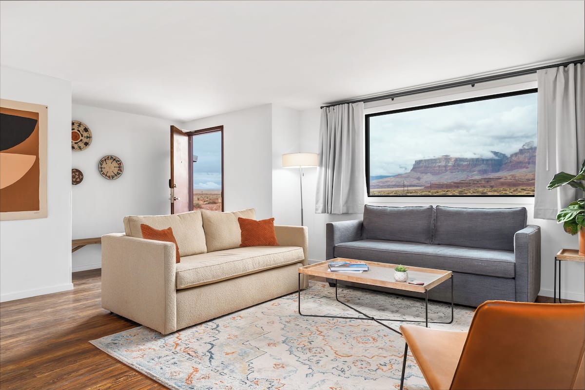 A modern living room with two sofas, a coffee table, and a large window with a mountain view.