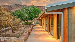 Un edificio moderno con un sendero de piedra que conduce a una puerta de madera, sobre un paisaje desértico con montañas al fondo.