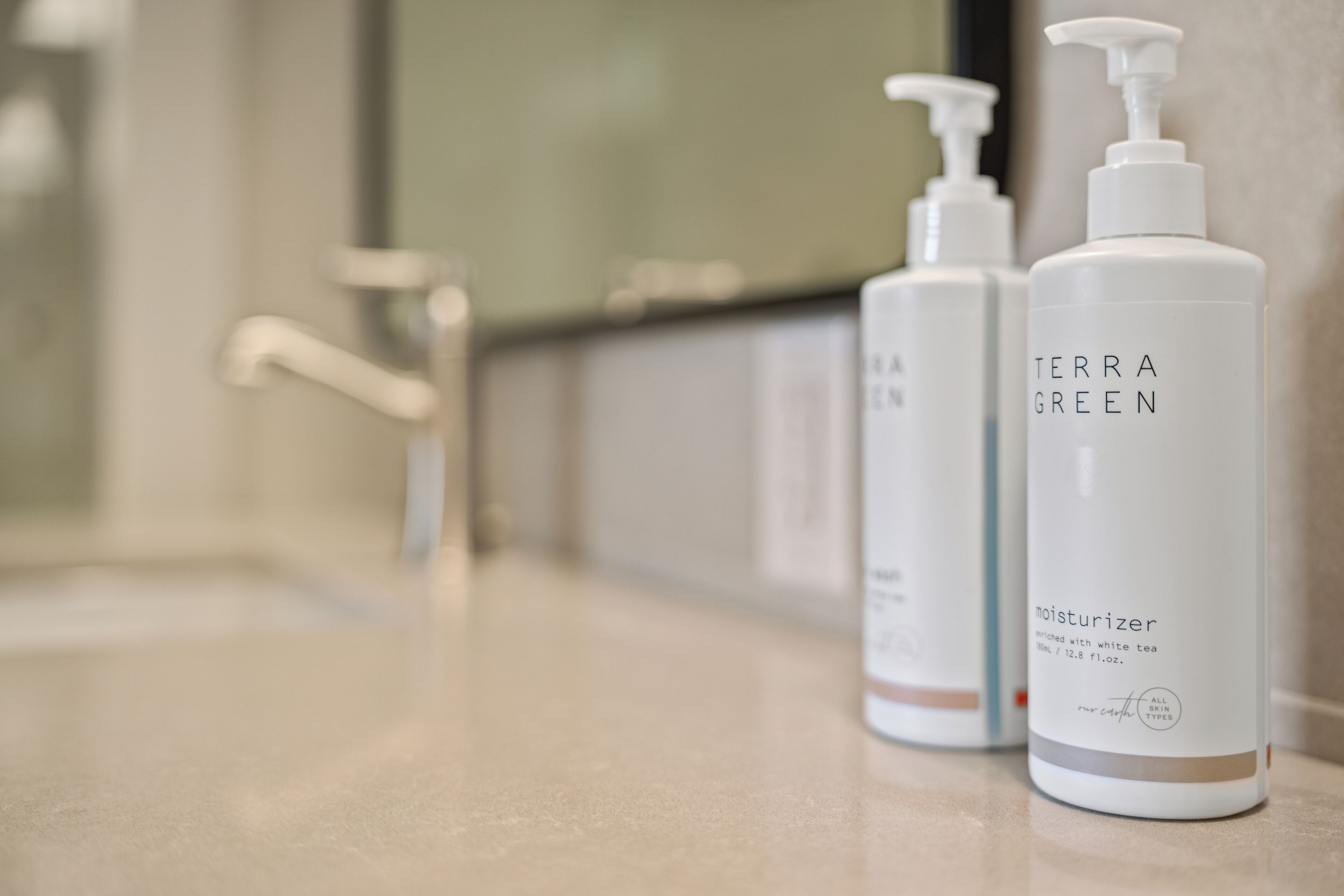 A bathroom with a white countertop, a mirror, and two bottles of Terra Green moisturizer.