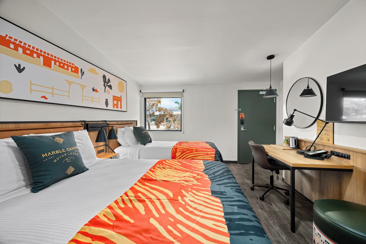 A hotel room with a bed, a desk, and a chair. There is a window with a view of trees and a door.