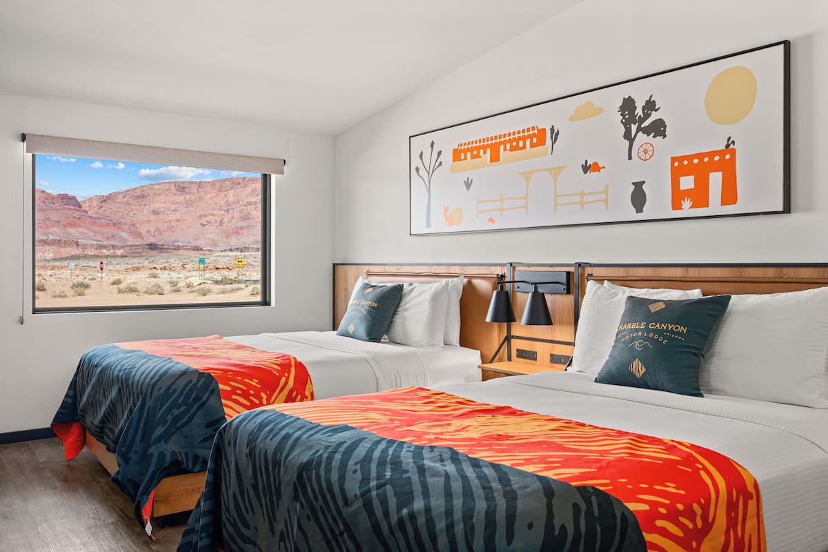 A hotel room with two beds, a large window with a desert view, and a wall art depicting a desert scene.