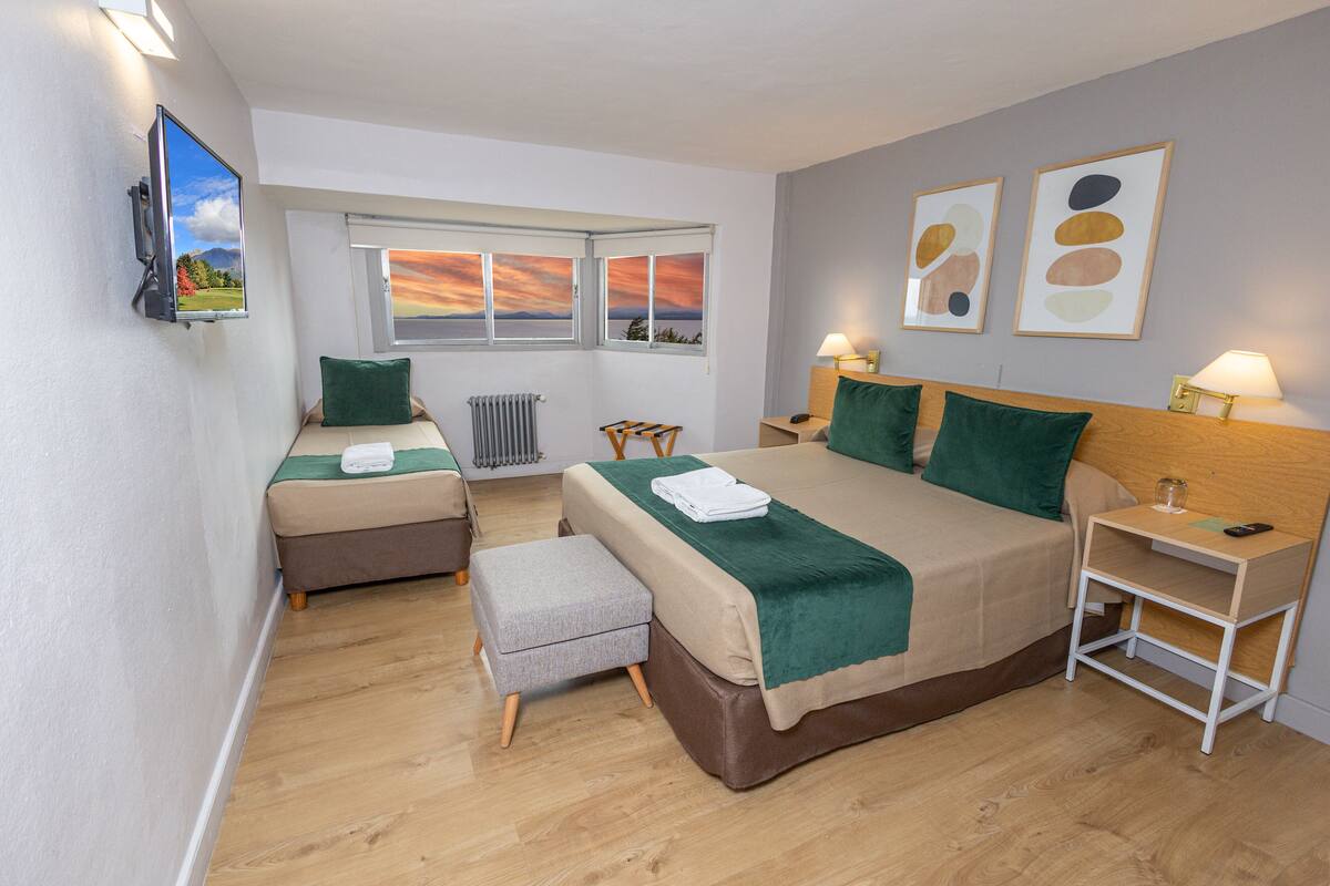 Ein Hotelzimmer mit einem großen Bett, einem Einzelbett, einem Fernseher, einem Fenster mit schöner Aussicht und einem Nachttisch mit Lampe.