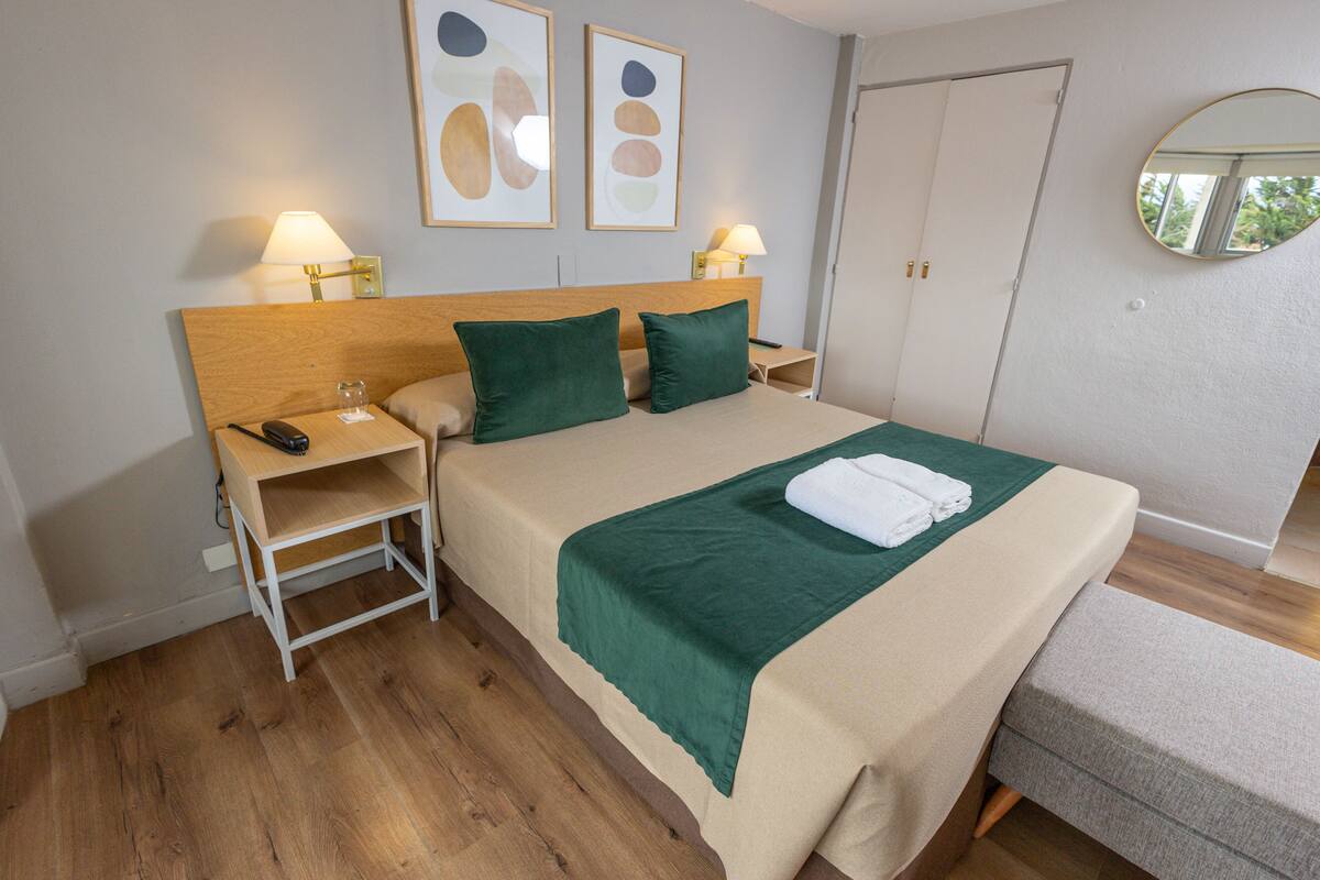 Ein ordentlich eingerichtetes Hotelzimmer mit Bett, Nachttischen, Lampen und Bildern an den Wänden.