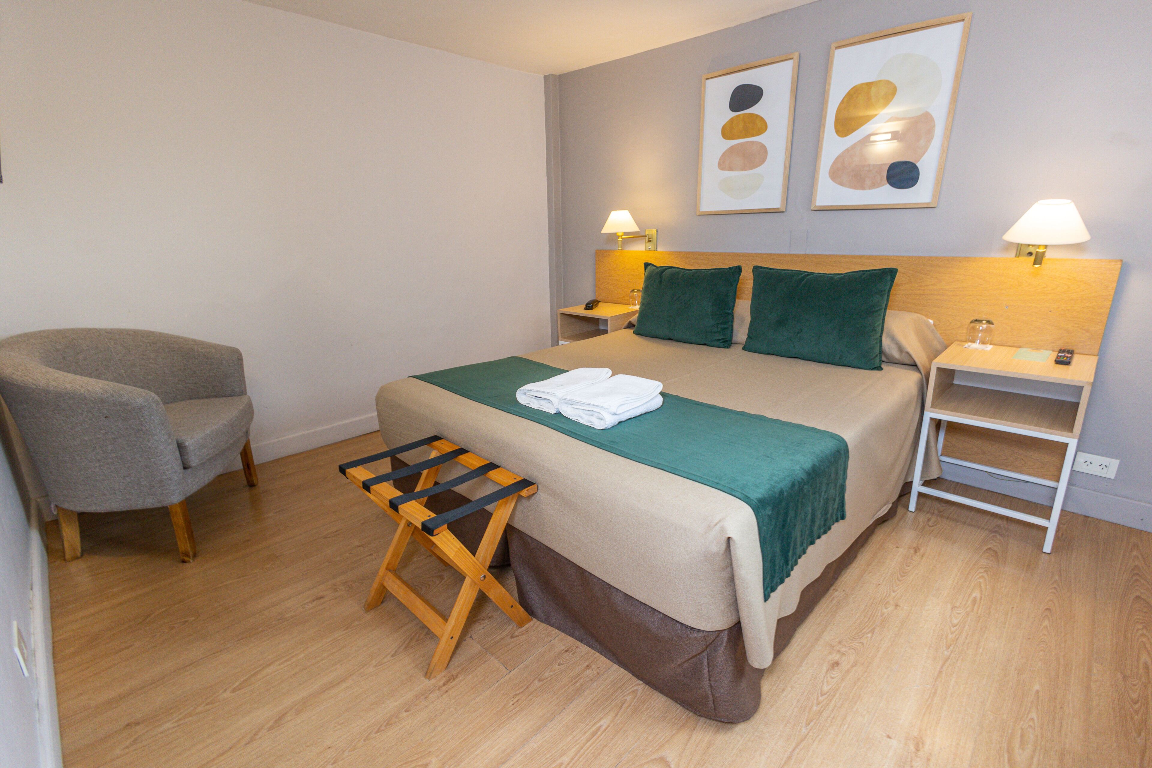 Ein ordentlich eingerichtetes Hotelzimmer mit einem Bett, einem Sessel, einem kleinen Tisch und einer Bank.
