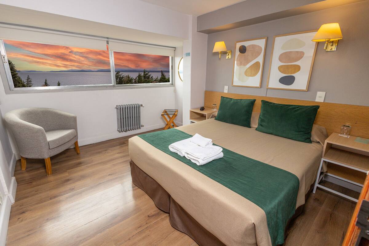 Ein Hotelzimmer mit Bett, Sessel, Meerblick und Bildern an der Wand.