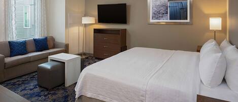 A hotel room with a bed, a sofa, a desk, a TV, and a picture on the wall.