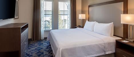 A hotel room with a large bed, two bedside lamps, a flat-screen TV, a desk, and a window with curtains.