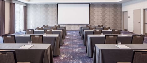 A conference room with tables and chairs, a projector screen, and patterned wallpaper.