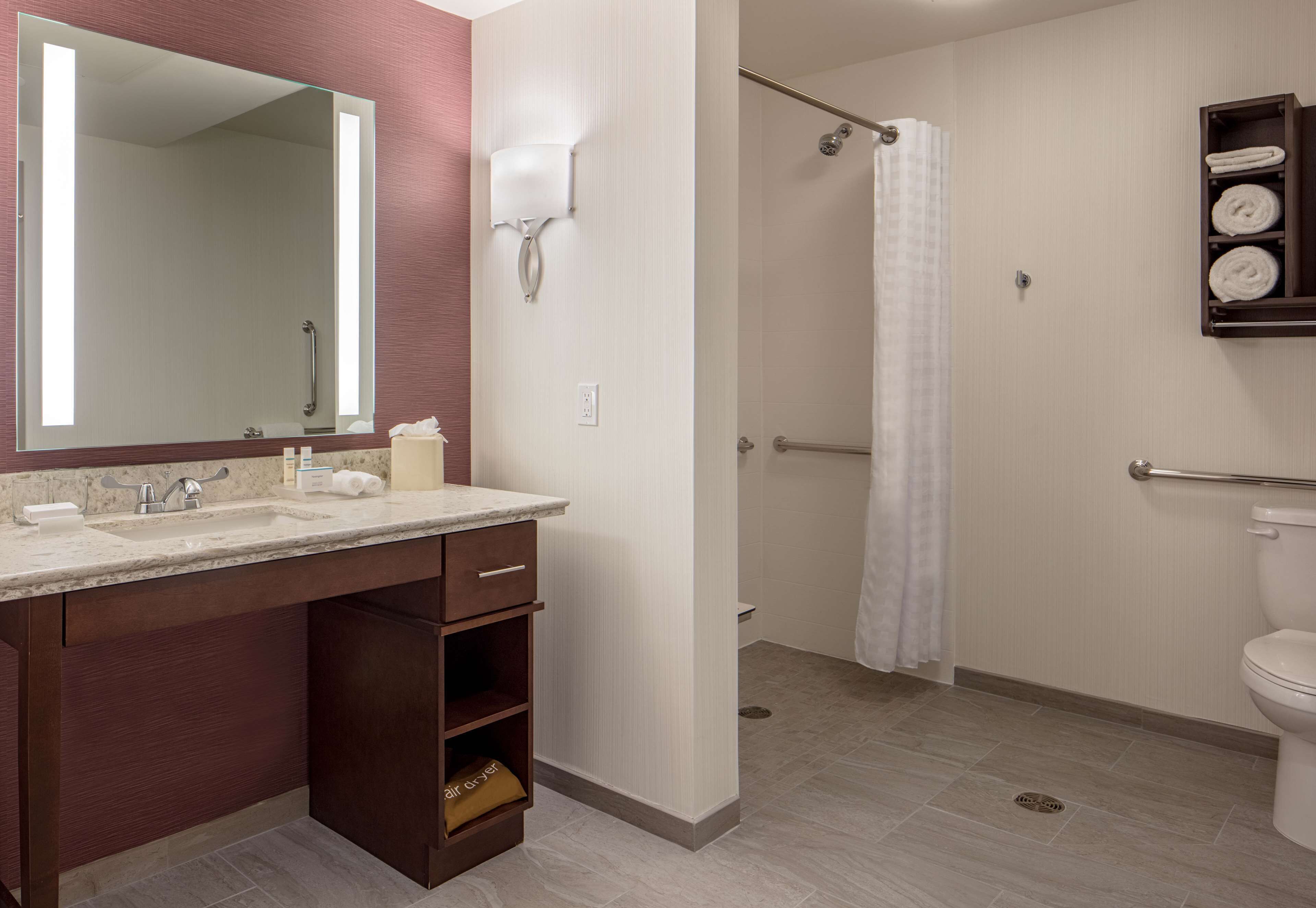 A modern bathroom with a double sink vanity, a large mirror, a shower with a glass door, and a toilet.