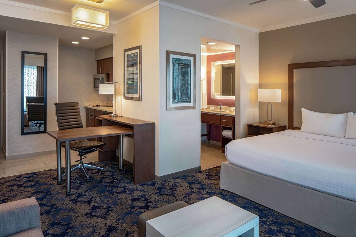 A hotel room with a bed, desk, chair, and a small table.