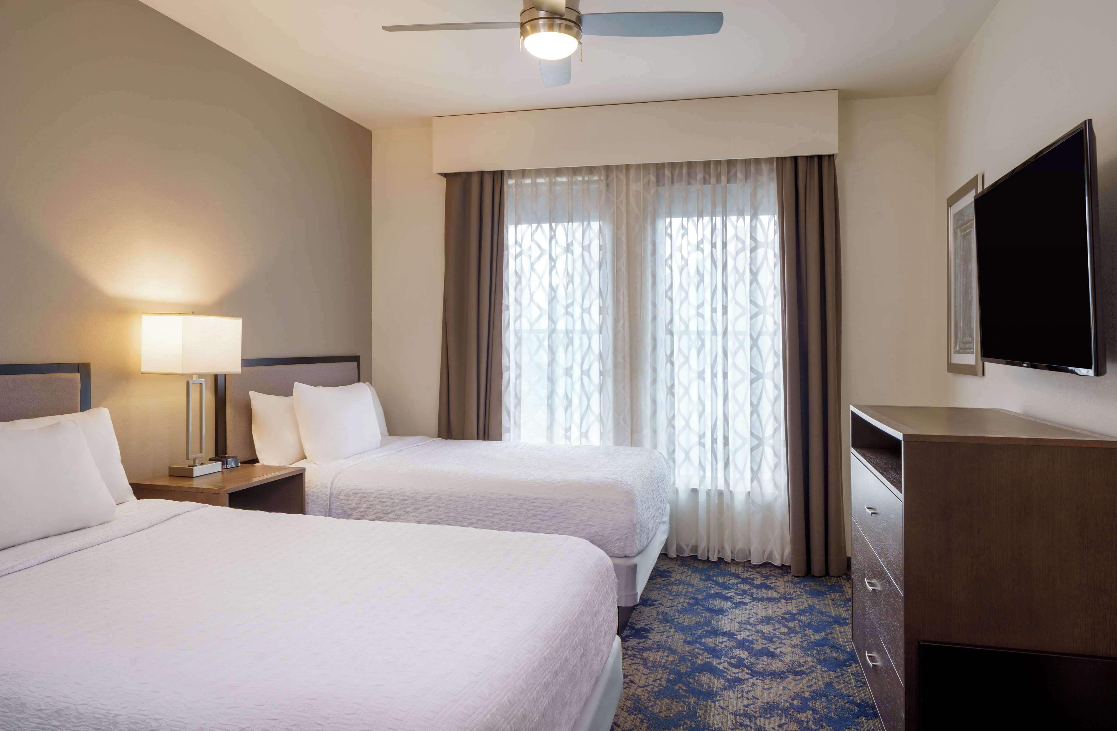 A hotel room with two beds, a ceiling fan, a TV, and a desk with drawers.