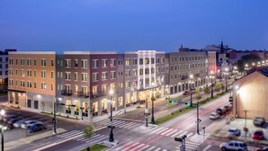 A multi-story hotel with a modern facade, a parking lot, and a street view with traffic lights and cars.