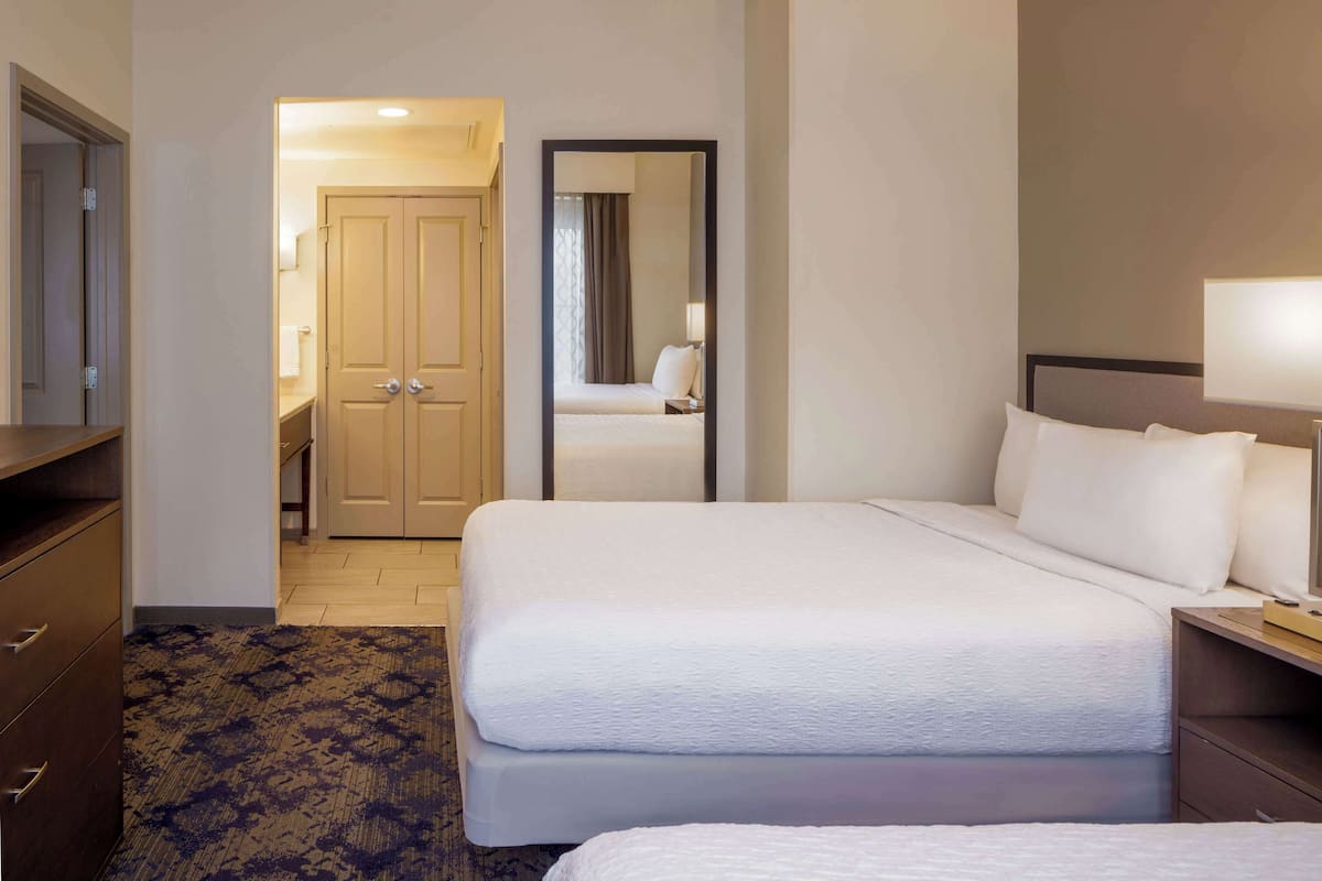 A hotel room with a large bed, a bedside table with a lamp, a wardrobe, and a carpeted floor.