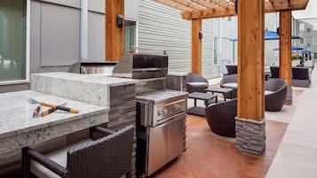 Un área de cocina al aire libre con una parrilla empotrada, asientos y una estructura de pérgola.