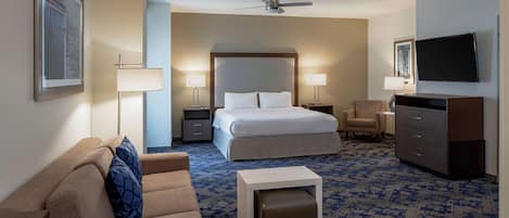 A hotel room with a large bed, a sofa, a desk, a TV, and a ceiling fan.