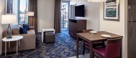 Une chambre d’hôtel comprenant un canapé, une petite table, une table à manger avec des chaises, un téléviseur et un réfrigérateur.