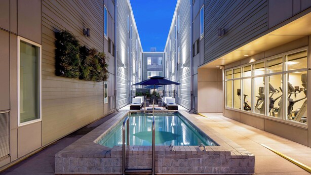 An indoor swimming pool with a view of the sky, surrounded by walls with windows and exercise equipment.