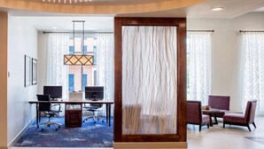 A modern hotel room with a desk, office chairs, a large window, and a decorative wall panel.