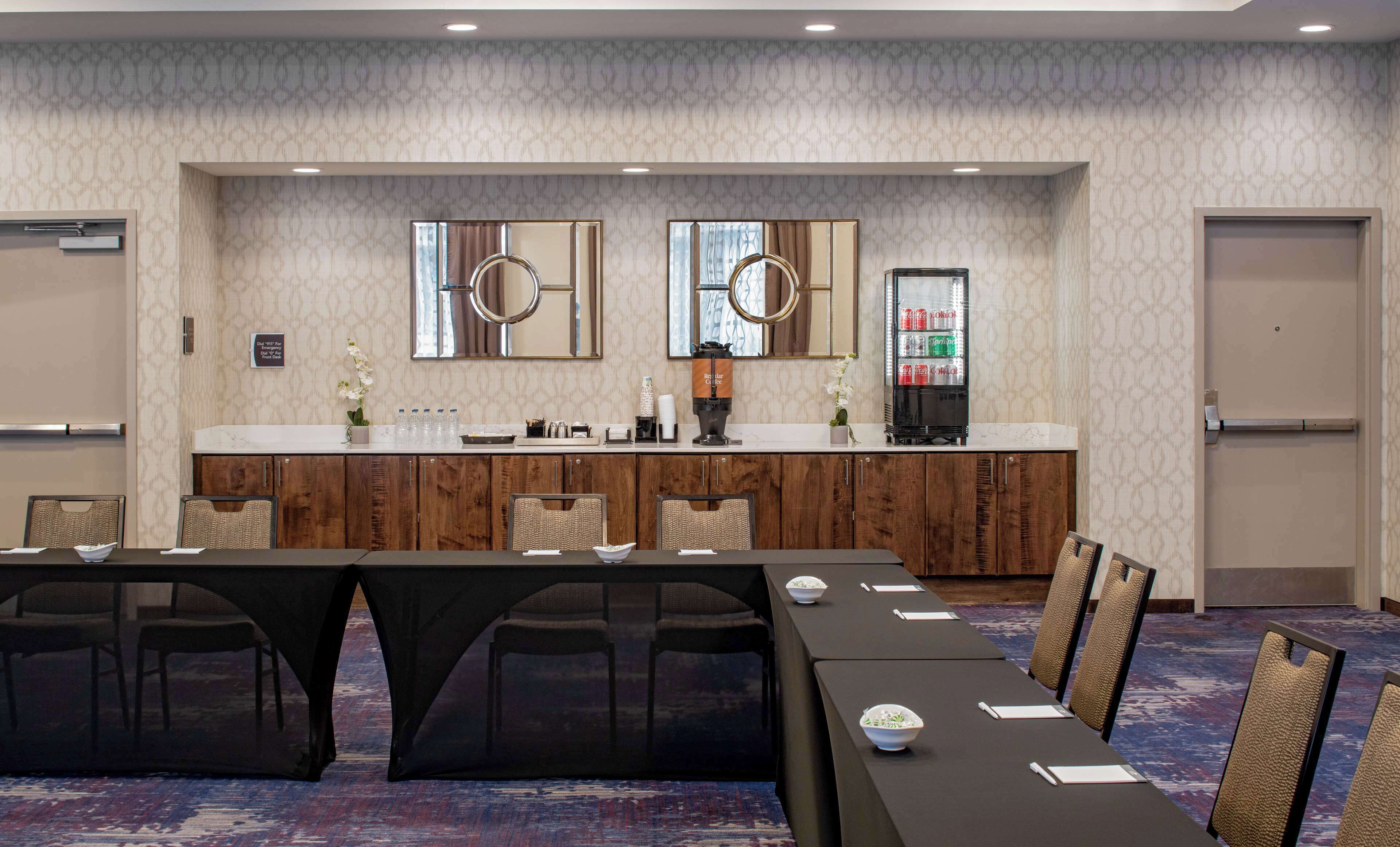 A conference room with a long table, chairs, a coffee station, and a refrigerator.