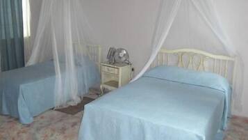 A bedroom with two single beds, each with a canopy, a bedside table with a lamp, and a floral-patterned carpet.