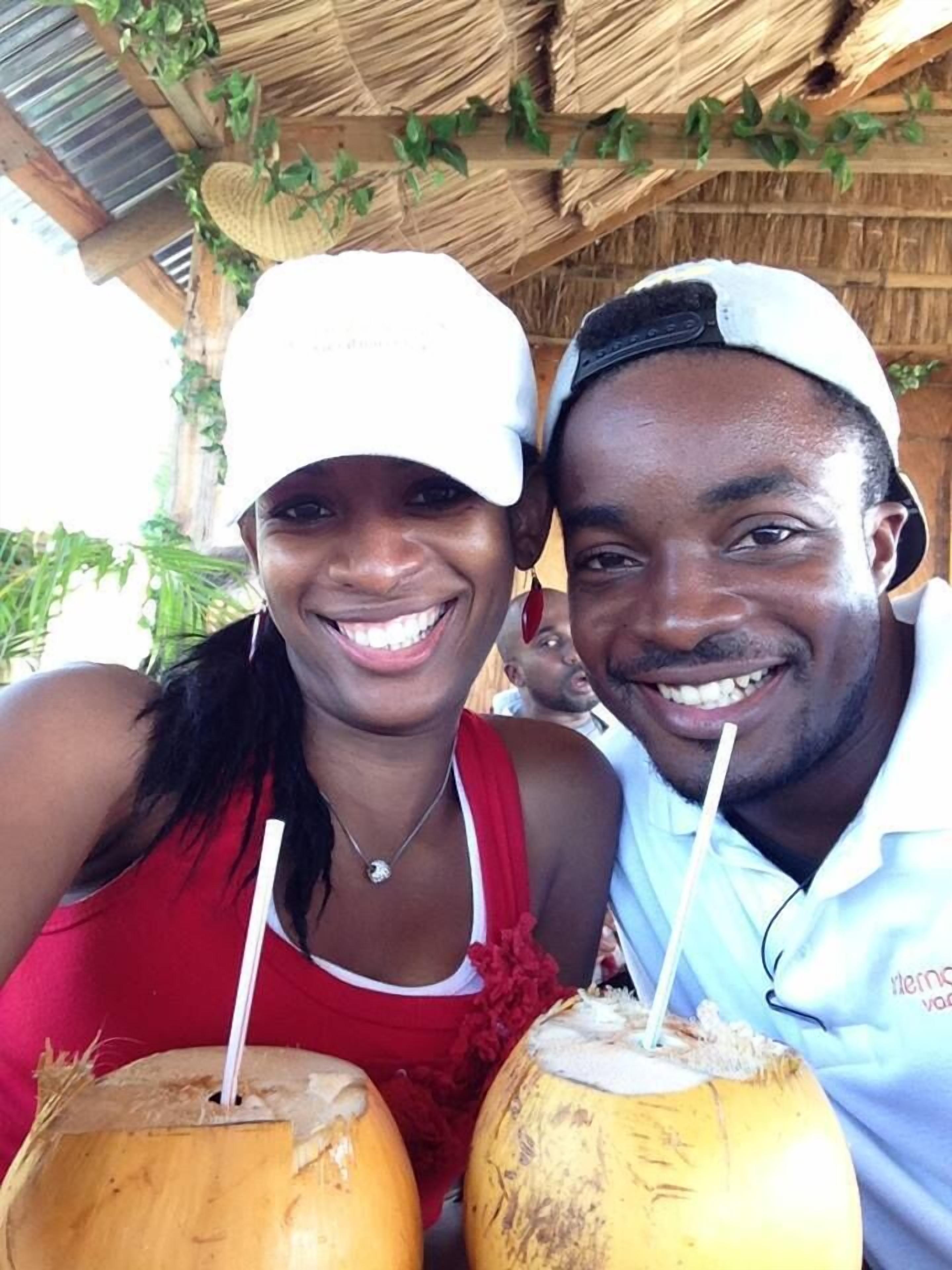 A couple holding coconuts with straws, under a thatched roof structure.
