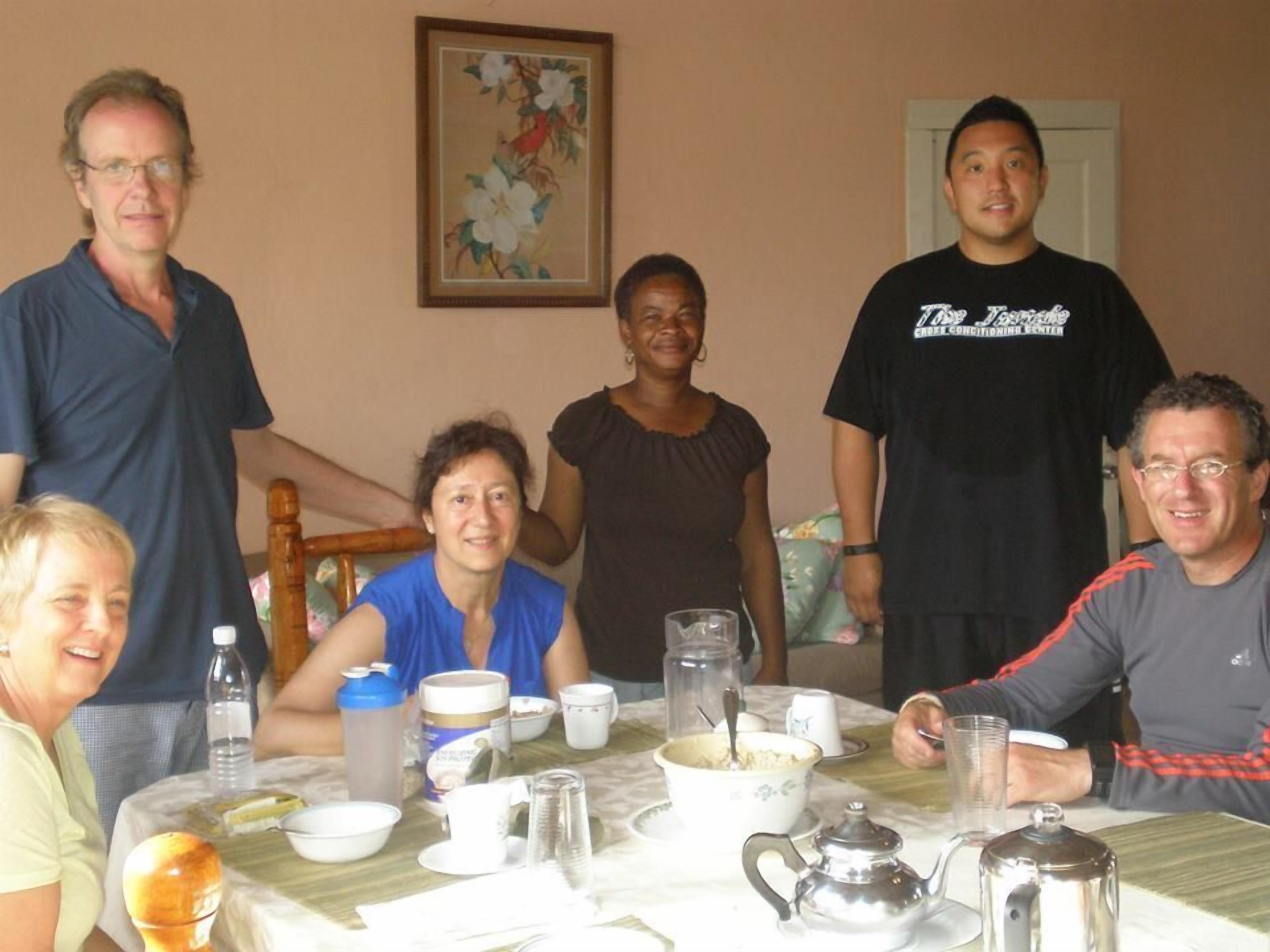 A group of people seated around a table with various dishes and drinks, in a room with a painting on the wall.
