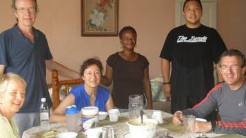A group of people seated around a table with various dishes and drinks, in a room with a painting on the wall.