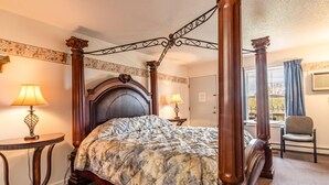 A four-poster bed with a floral bedspread, two bedside lamps, a small round table, and a chair in a hotel room. - Gateway Inn (Medway)