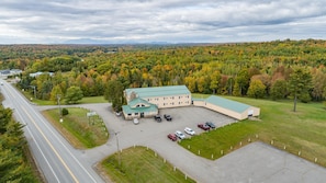 An aerial view of a large building with a green roof, surrounded by a parking lot and a road.