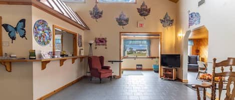 Een ruime lobby met hoog plafond, houten balken, een receptiebalie, een rode fauteuil, een televisie en uitzicht op het omliggende landschap door grote ramen.
