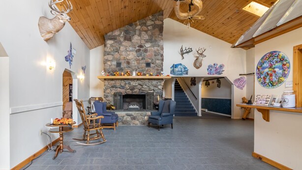 A spacious living area with a stone fireplace, wooden ceiling, and rustic decor including deer antlers and a chandelier. - Gateway Inn (Medway)