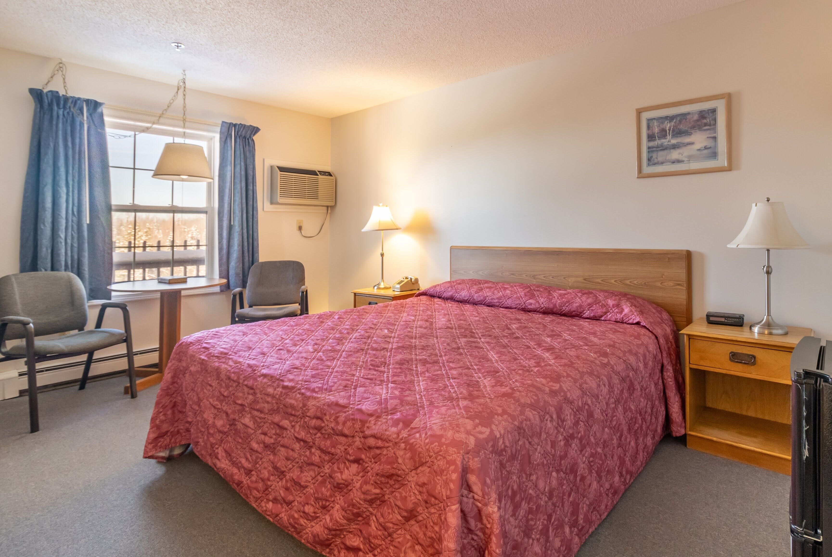 A neatly arranged bedroom with a large bed, two chairs, a desk, and a window with curtains.