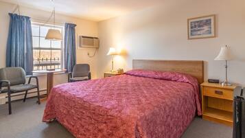 A neatly arranged bedroom with a large bed, two chairs, a desk, and a window with curtains.